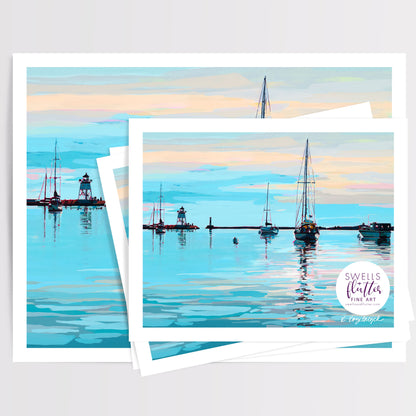 A stack of art prints showing a painted Grand Marais, MN harbor scene with sailboats, a lighthouse, and calm blue water under a pastel sky. A circular logo in the lower right reads 'Swells + Flutter Fine Art'. Artwork by Kristen Kozelouzek.